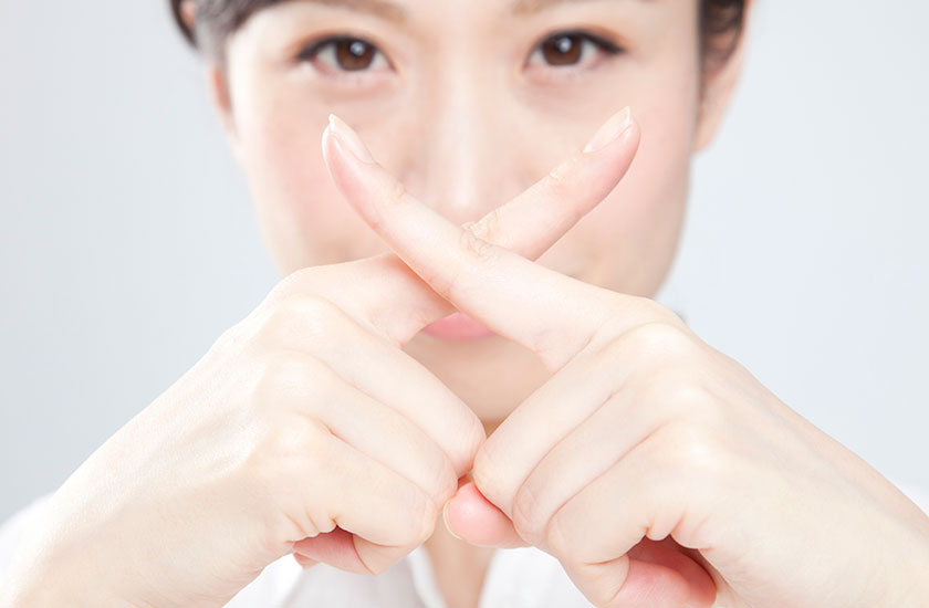 指でバツ印をつくる女性